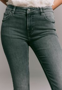 Kõrge vöökohtaga hallid denim püksid, millel on kitsas lõige, viis taskut, üksnuppude sulgemine ja peened õmbluse detailid.