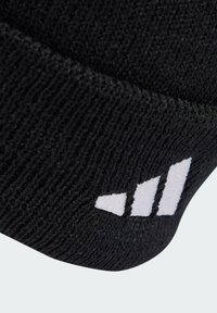 Beanie in maglia nera con una texture a coste e un logo a tre strisce bianche su un lato, caratterizzato da una silhouette affusolata nella parte superiore.