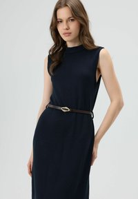 Mouwloze marineblauwe jurk met een gestructureerd patroon, ceintuurlus met een bruine riem met een gouden accent. Simpel, elegant ontwerp.