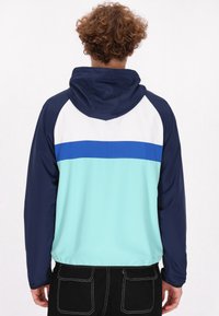 Hoody-jack met een kleurblokontwerp in marineblauw, wit en lichtturquoise, met een elastische taille en een gladde textuur.
