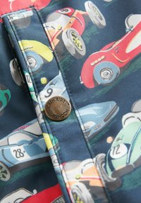 Tissu multicolore avec des voitures de course au style cartoon dans différentes couleurs. Comprend un bouton en bronze gravé "CATH KIDS LONDON".