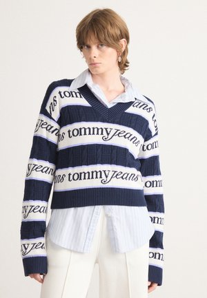 Mørkeblå strikkegenser med hvite og lysblå striper som har "tommy jeans"-tekst, V-halsdesign og grov tekstur.