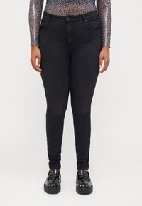 Black skinny jeans made of denim with a smooth texture, featuring five pockets and a mid-rise waist. Worn with chunky black loafers.