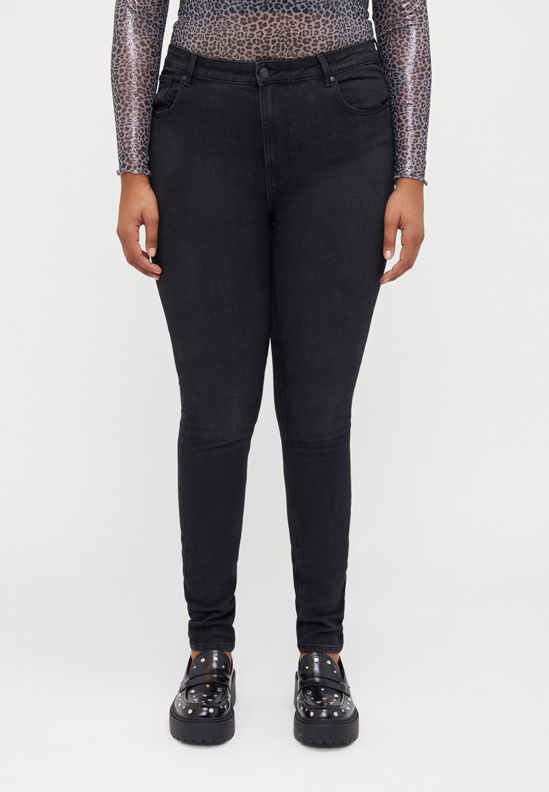 Black skinny jeans made of denim with a smooth texture, featuring five pockets and a mid-rise waist. Worn with chunky black loafers.