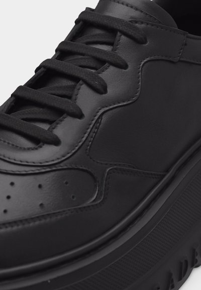 Baskets en cuir noir avec semelle en caoutchouc épaisse, panneaux cousus, perforations près des orteils et lacets noirs attachés sur une languette rembourrée.