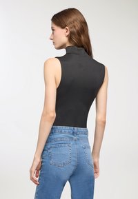 Body aderente nero senza maniche con scollatura alta, abbinato a jeans azzurri a vita alta con tasche posteriori e un lavaggio sbiadito.