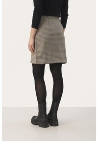 Brun och beige rutad kjol med en figursydd midja, tillsammans med svarta strumpbyxor och kraftiga svarta ankelstövlar. Slät textur, ovanför-knä längd.