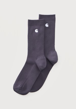 Paire de chaussettes côtelées gris foncé avec un logo brodé blanc près du bord supérieur sur un fond clair uni.