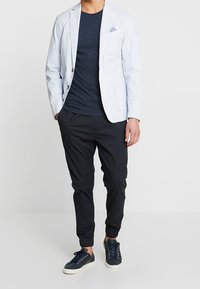 Blazer azul claro con dos botones, un pañuelo de bolsillo, combinado con una camiseta oscura y pantalones negros ajustados, terminado con zapatillas azul marino.