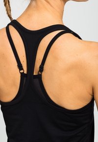 Černý bezrukávový top s designem na závodní záda, nastavitelnými ramínky a hladkým, elastickým materiálem.