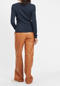 Mörkblå tröja med lång ärm och rund halsringning, tillsammans med ljusa läderbyxor med en slät textur och rak passform.