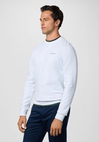 Sudadera blanca de manga larga, con puños de canalé y un acento verde en el cuello. Presenta un pequeño logo de "Hackett" en el pecho.