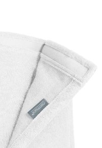 Weißes Baumwollhandtuch mit strukturierter Oberfläche. Verfügt über eine umgeschlagene Ecke mit einem grauen Etikett und einem Klettverschluss. Einfaches und funktionales Design.