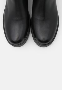 Musta nahkasaappaat nilkkapituisilla, sileällä pinnalla, pyöreällä varvaskärjellä ja paksulla kumipohjalla, suunniteltu kestävyys ja mukavuus mielessä.