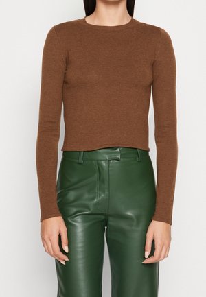 Pull marron à manches longues en matériau doux, avec un col rond et un design légèrement court, associé à un pantalon en cuir vert.
