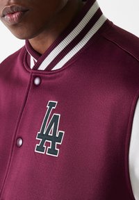 Burgunderfarget varsityjakke med hvit og stripete krage, knappelukking og svart LA-logo brodert på brystet.