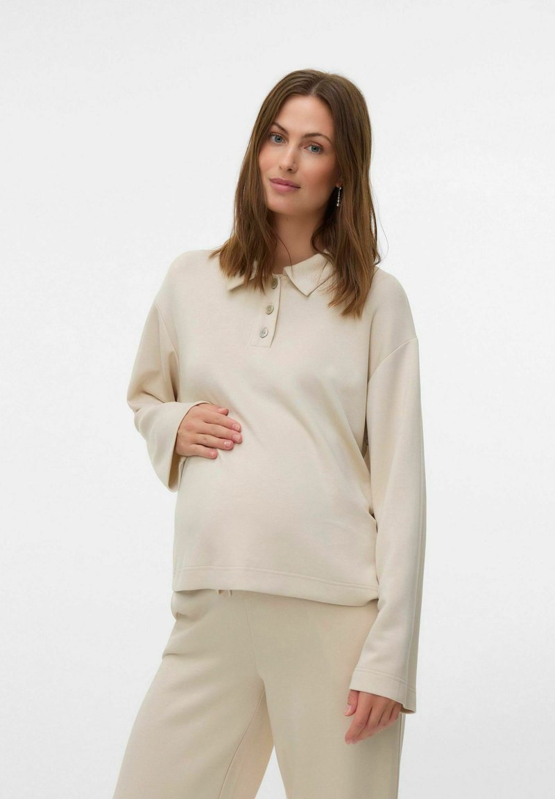 Beżowy sweter z kołnierzykiem, z trzema guzikami. Wykonany z miękkiego materiału, ma luźny krój i długie rękawy. Połączony z pasującymi spodniami.