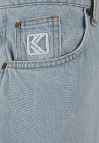 Jeans in denim di colore azzurro chiaro con una finitura testurizzata. Presentano un logo ricamato bianco sulla tasca posteriore e dettagli in cucitura di contrasto.
