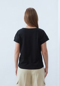 Svart kortärmad t-shirt med rund halslinning, mjuk textur, avslappnad passform. Matchad med beige vida byxor.