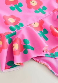 Tessuto da bagno rosa con un motivo di fiori in rosso, giallo e verde, con orlo arricciato e texture liscia.