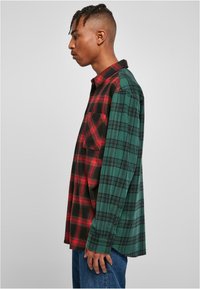Rood en zwart geruit patroon aan de ene kant, groen en zwart geruit aan de andere kant. Het stof is flanel, met lange mouwen en een oversized pasvorm. Heeft een knoopsluiting aan de voorkant.