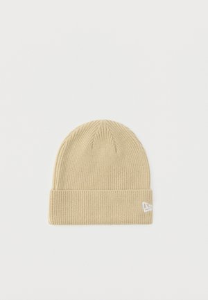 Bonnet beige tricoté avec revers plié et petit logo blanc cousu sur le revers, présenté sur un fond blanc uni.