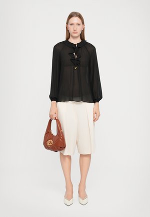 Blusa nera trasparente con dettagli a ruches, abbinata a pantaloni corti plissettati di colore chiaro. Accessoriata con una borsa marrone e tacchi bianchi a punta.
