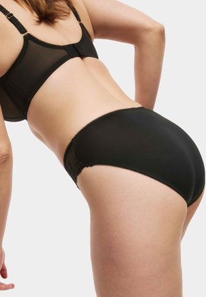 Zwart lingeriesetje met een doorschijnende mesh beha met gouden accenten en een bijpassende zwarte slip met kantdetails en golvende randen.