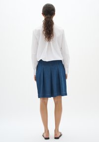 Modra jeans krilo s pliseji, do kolen, in dekorativnim robom, v kombinaciji z belo srajco z dolgimi rokavi. Preprost dizajn z minimalno kovinsko opremo.