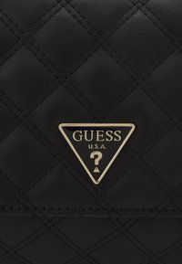 Borsa sintetica nera trapuntata con logo triangolare dorato con la scritta "GUESS" e "U.S.A." su uno sfondo testurizzato.
