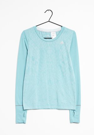 Jasnoniebieska sportowa koszulka Adidas z długim rękawem, z subtelnym wzorem i otworami na kciuki na mankietach, zawieszona na czarnym wieszaku na białym tle.