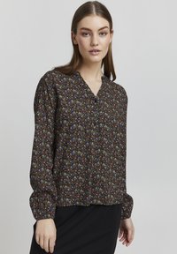 Svart bluse med blomsterprint i flere farger. Har V-hals og lange pufferm med tettsittende mansjetter. Lett stoff.