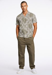 Camisa de manga corta, color verde oliva, con estampado floral blanco, combinada con pantalones khaki de corte holgado y zapatillas blancas.