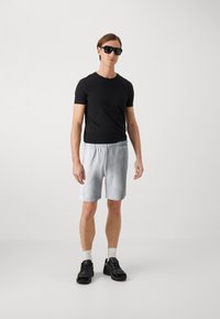 Schwarzes T-Shirt mit kurzen Ärmeln, hellgraue Shorts und schwarze Sneaker. Das Modell trägt Sonnenbrillen und weiße Socken; glatter Stoff, elastischer Bund.