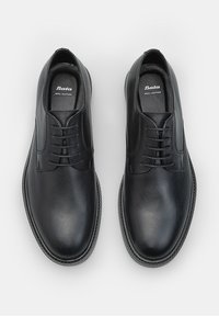 Zapatos de cuero negro con un acabado suave, con punta redondeada, diseño de cordones y sutilezas en la costura. Logotipo "Bata" visible en el interior.