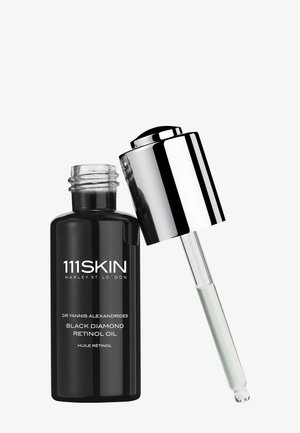 Schwarze Glasflasche mit der Aufschrift Black Diamond Retinol Oil, an die ein silberner Tropfer auf weißem Hintergrund lehnt.