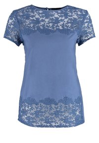 Haut bleu à manches courtes avec un motif en dentelle florale sur le corsage et l'ourlet, et un tissu lisse en dessous.
