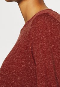 Roter melierter Sweatshirt mit rundem Ausschnitt und strukturiertem Stoff, mit sichtbaren Nähdetails entlang der Schulternaht.