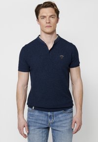 Tumši zila īsām piedurknēm polo krekls ar teksturētu audumu, ar henley jaka un baltajiem akcentiem. Mazi logotips uz krūtīm.