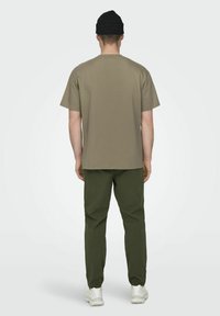 Camiseta de manga corta color caqui hecha de algodón, combinada con pantalones en color verde oliva. El modelo lleva un gorro negro y zapatillas blancas.