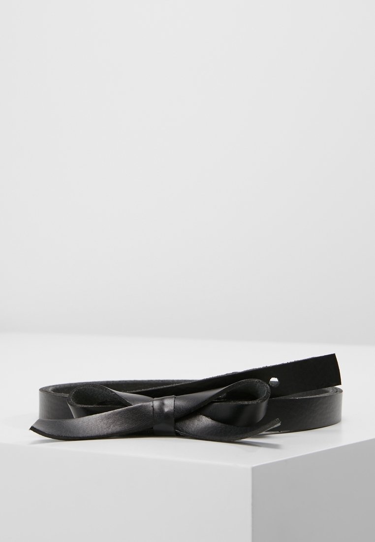 Ceinture en cuir noire avec un détail simple en forme de nœud, posée à plat sur une surface blanche sur fond gris clair.