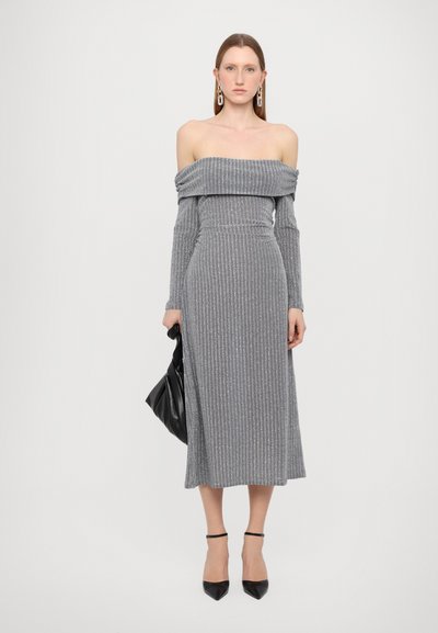 Rochie maxi gri, cu umerii descoperiți, cu dungi, mâneci lungi, dintr-un material texturat și cu talie ajustată. Modelul ține o geantă neagră și poartă tocuri negre.