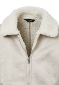 Giacca in suede beige con un morbido colletto in finta shearling bianco, chiusura con zip integrale e una fodera interna soffice e testurizzata.