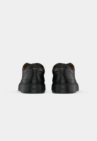 Pair of black leather sneakers with "BOSS" embossed on the back heel, shown from rear view on a plain white background.
