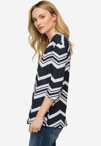 Top s námořnickým a bílým vzorem chevron, s tříčtvrtečními rukávy, kulatým výstřihem a volným střihem, vyrobený z lehkého materiálu.