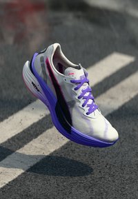 Chaussure de course légère avec une tige en mesh blanche et grise ornée d'accents violets, d'une bande noire et de lacets violets. Semelle texturée pour une meilleure adhérence.
