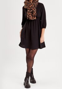 Robe noire à manches trois-quarts avec une taille cintrée, accompagnée d'une écharpe marron à imprimé léopard. Bottines noires à semelles épaisses.