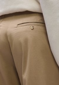 Bézs színű, sima textúrájú pamut nadrág, hátul zsebbel és gombos rögzítéssel. A derékrész szépen befejezett.