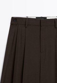 Pantalons tailleur marron avec devant plissé, fermeture à bouton, passants de ceinture et détails brodés, réalisés en tissu lisse.
