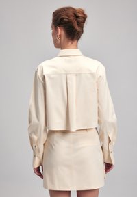 Lichtcrème kleurige cropped shirt met lange mouwen en een plooi aan de achterkant, gecombineerd met een bijpassende rok met hoge taille. Soepele textuur.
